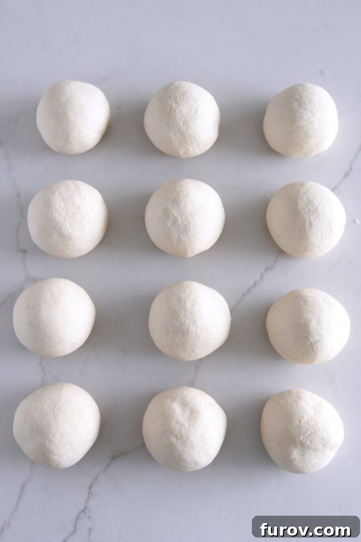 12 perfectly rounded dough balls resting on a white counter.