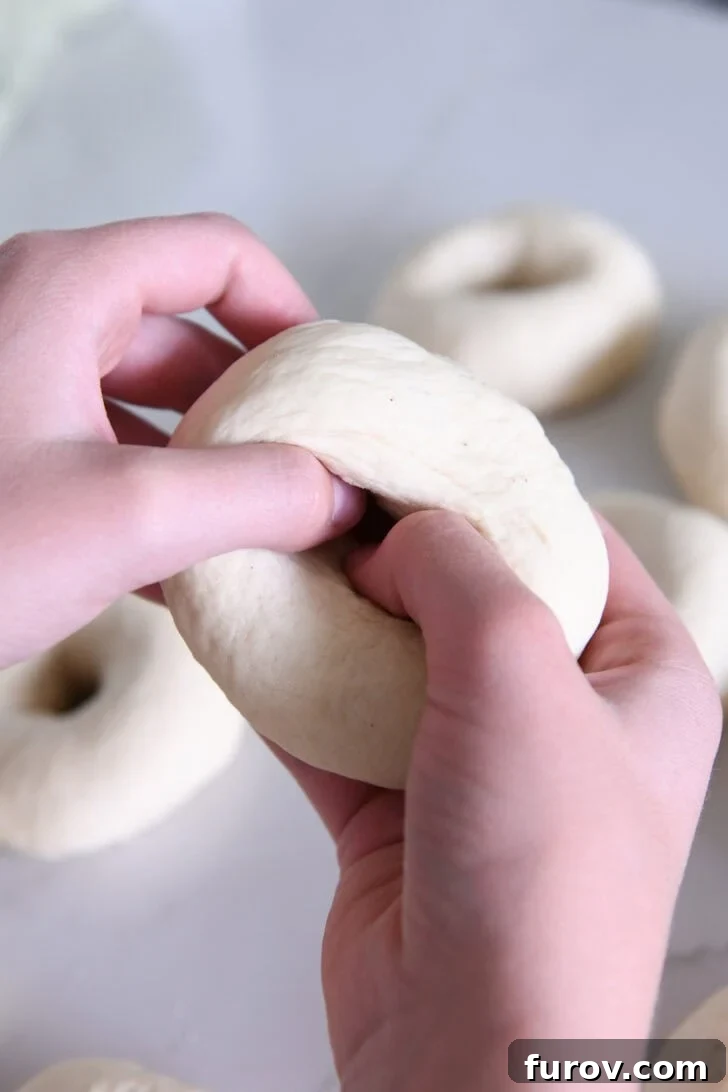 Hands pressing thumbs into a dough ball to begin forming the bagel hole.