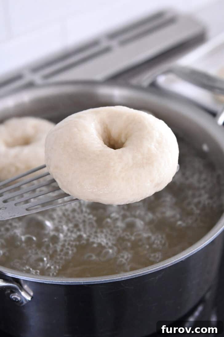 Lifting a perfectly boiled bagel out of the hot water with a stainless steel spatula, ready for toppings.