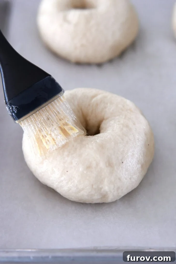 Brushing an egg wash onto a freshly boiled bagel before applying toppings.