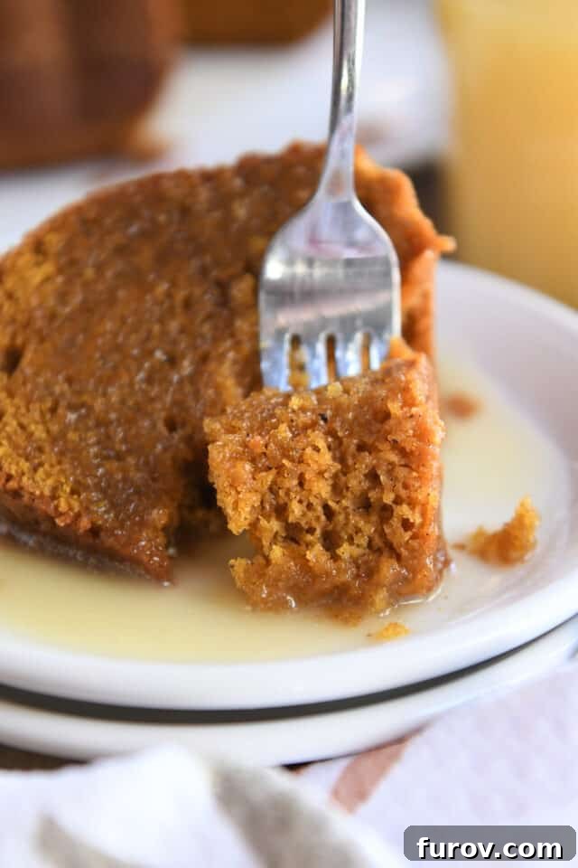Bite of orange pumpkin cake on fork on white plate, highlighting the cake's moist texture and rich color.