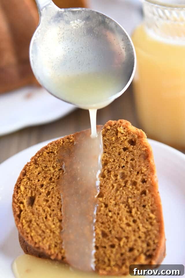 Small ladle spooning vanilla sauce over slice of pumpkin bundt cake on white plate, illustrating the luxurious drizzle.