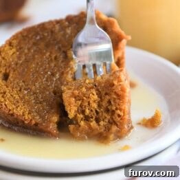 Bite of orange pumpkin cake being scooped out of big slice with fork on white plate, perfect for a recipe card image.