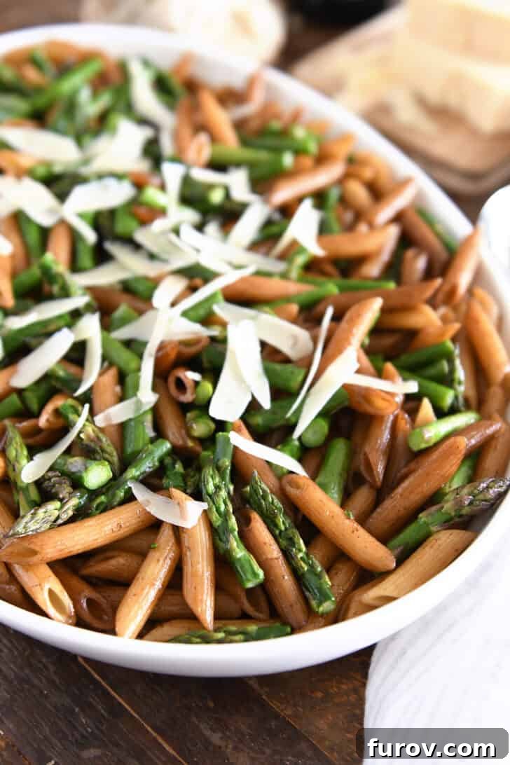 White serving dish with balsamic penne pasta, roasted asparagus and generous parmesan cheese.