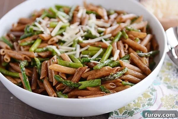 A large white bowl of balsamic-coated penne pasta and asparagus pieces with shredded parmesan on top.