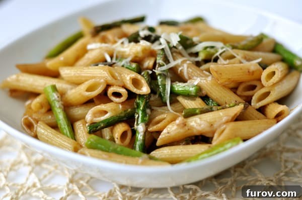 A white bowl of perfectly cooked penne pasta and crisp asparagus pieces, ready for the sauce.