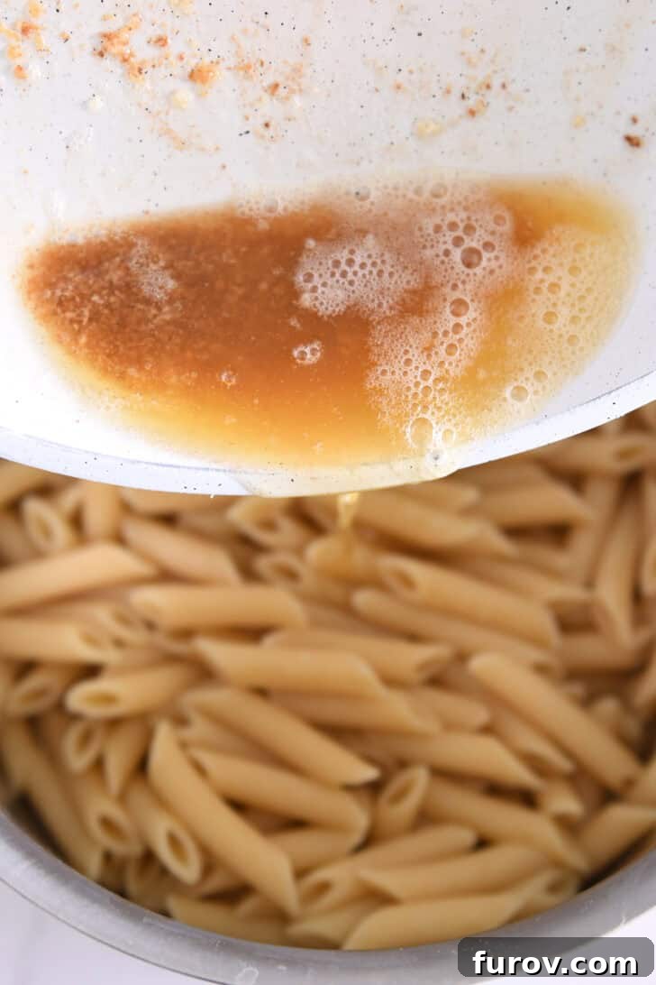 Rich brown butter being poured over freshly cooked penne pasta.