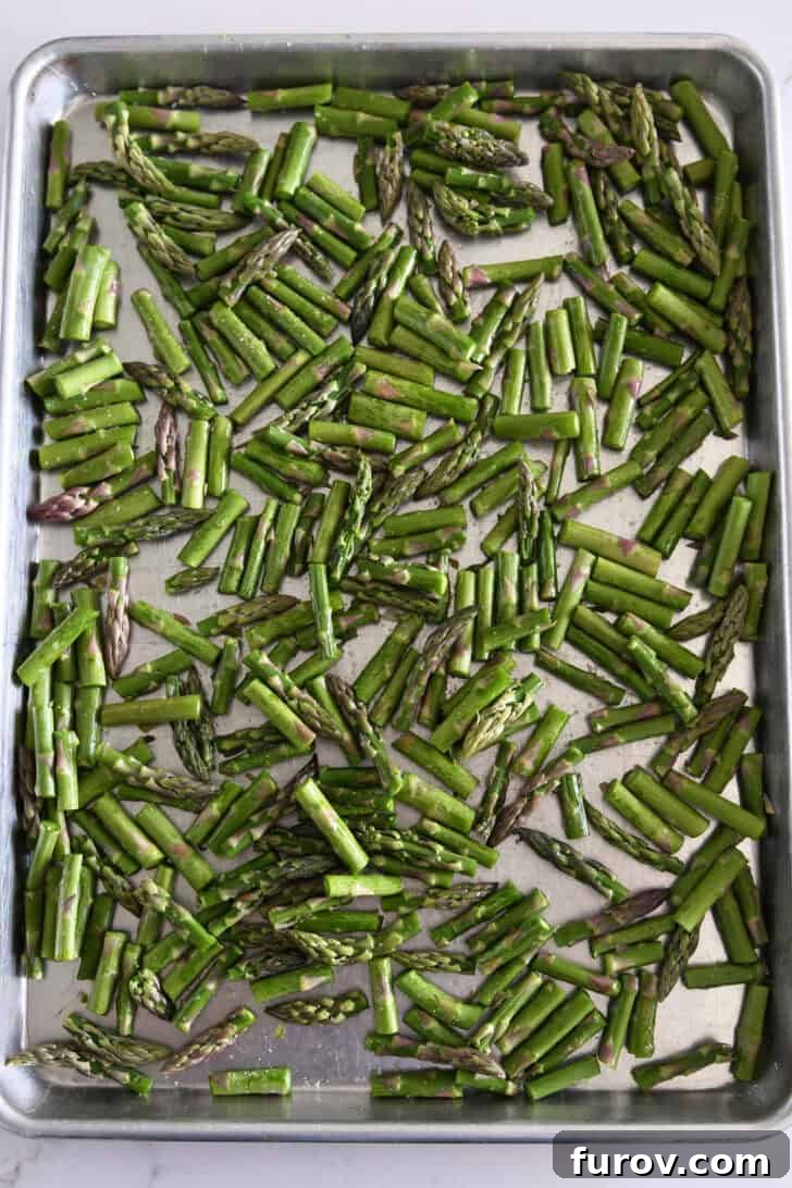 Fresh asparagus pieces seasoned with olive oil and salt on a baking sheet, ready for roasting.