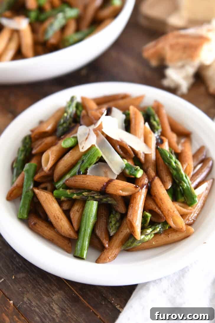 White plate showcasing balsamic drenched penne pasta, perfectly roasted asparagus, and a sprinkle of Parmesan cheese.