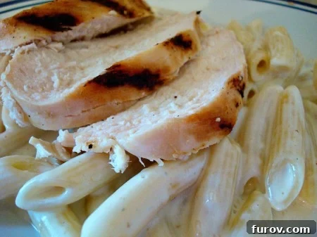 Grilled chicken strips and penne pasta coated in creamy gorgonzola sauce, garnished on a white plate.