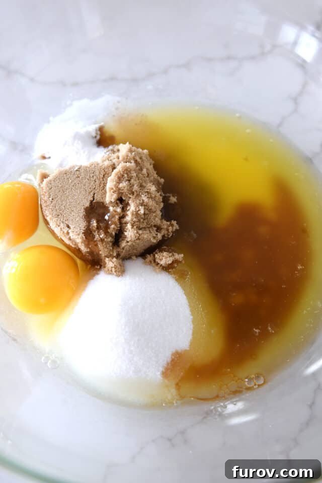 Homestyle Oatmeal Chocolate Chip Cookie Bars 3 Glass bowl containing white sugar, brown sugar, an egg, an egg yolk, and melted butter, ready for mixing.