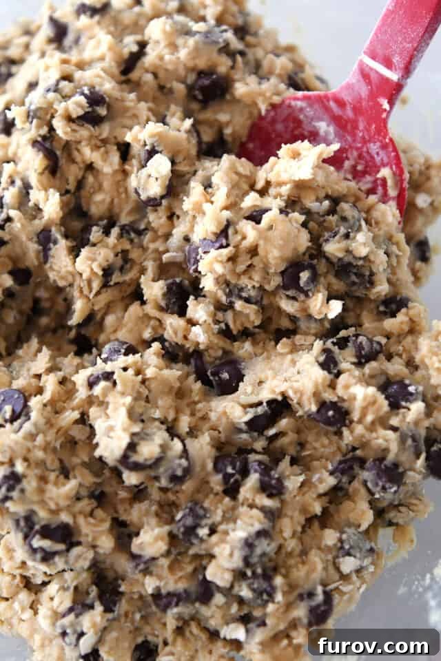 Homestyle Oatmeal Chocolate Chip Cookie Bars 5 Top down view of oatmeal chocolate chip cookie dough spread evenly in a glass bowl, showcasing its readiness for baking.
