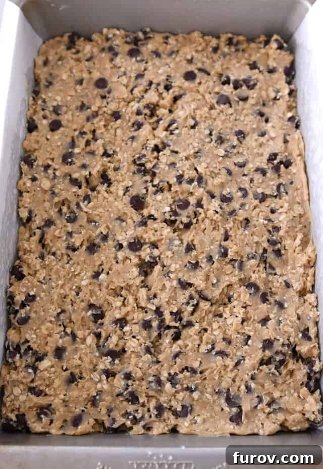 Homestyle Oatmeal Chocolate Chip Cookie Bars 6 9x13-inch baking pan filled with unbaked oatmeal chocolate chip cookie dough, smoothed and ready for the oven.