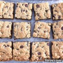 Twelve squares of cut chocolate chip cookie bars on white parchment paper, ready to be served.