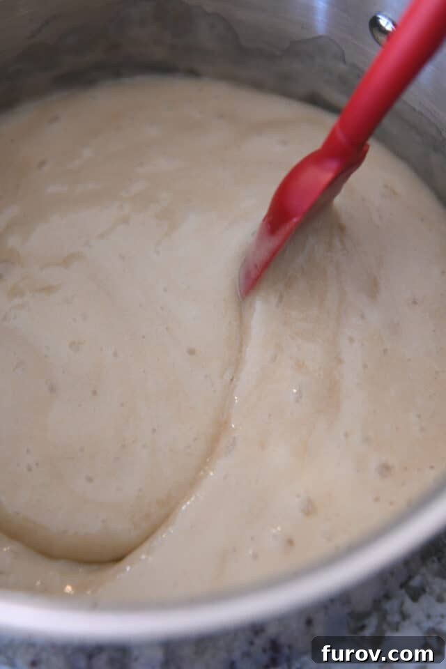 Velvety Buttermilk Caramel 6 Stirring syrup in saucepan with red spatula.