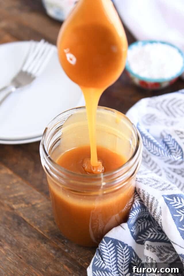 Velvety Buttermilk Caramel 7 Wooden spoon drizzling caramel syrup into glass jar.