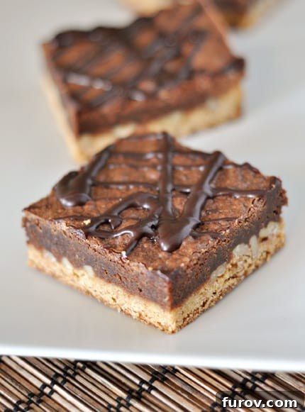 A perfectly cut square Congo Bar, showcasing its distinct blondie base, rich brownie top, and an elegant ganache drizzle across the surface, highlighting its layered deliciousness.