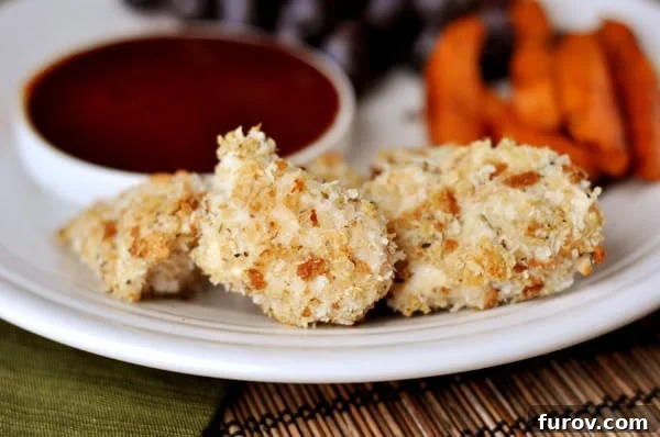 A white plate displaying several perfectly golden-brown homemade chicken nuggets, ready to be enjoyed with a bowl of dipping sauce in the foreground.