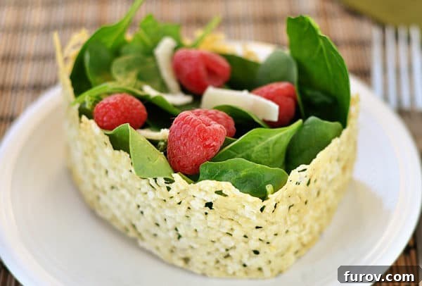 A vibrant spinach and raspberry salad beautifully presented in a golden-brown Asiago cheese crisp bowl, ready to be enjoyed.