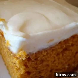 A close-up of a freshly baked pumpkin bar with a thick layer of cream cheese frosting, ready to be served.