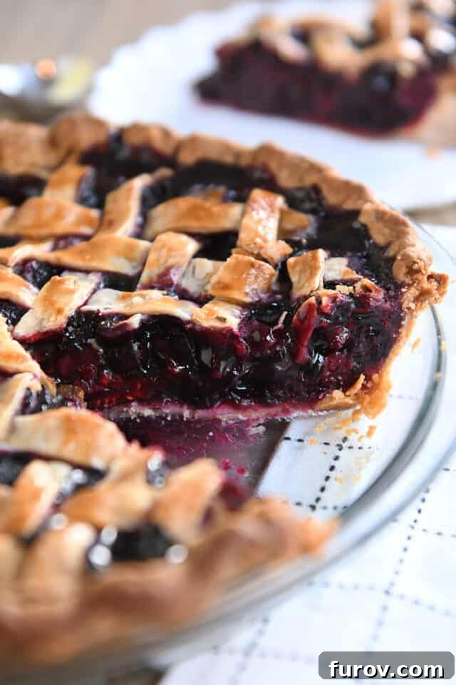 A beautifully baked triple berry pie in a glass pie plate, with one piece already removed, showcasing the vibrant berry filling and a perfectly golden lattice top crust.