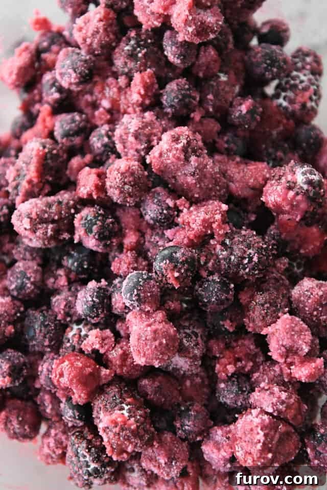 Close-up shot of frozen raspberries, blueberries, and blackberries mixed with granulated sugar and cornstarch in a glass bowl, ready for the pie filling.