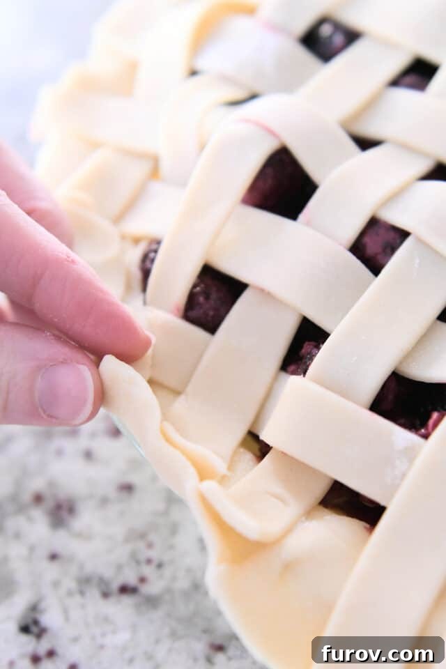 Detailed shot of the pie crust being folded over the lattice strips, securing the edges of the unbaked triple berry pie.