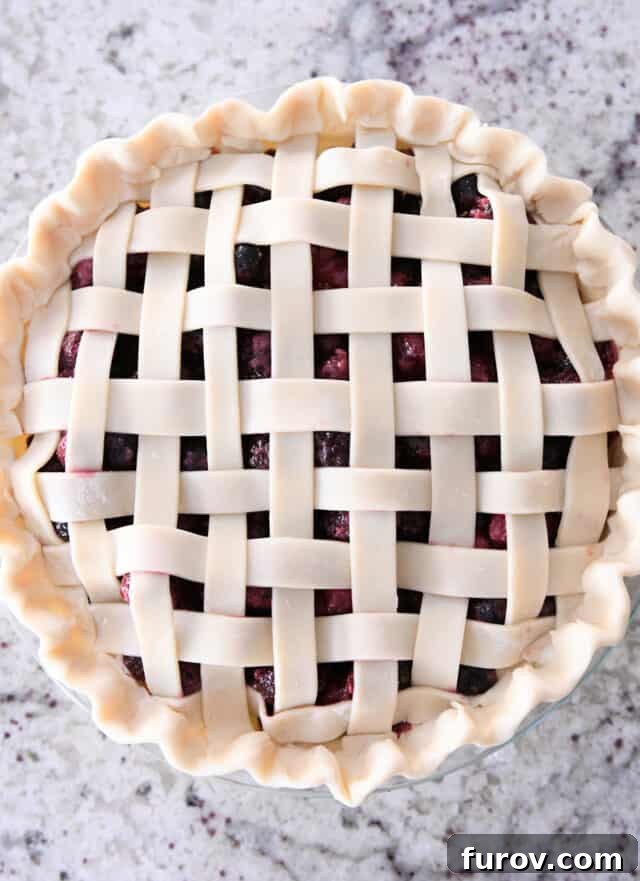 A stunning unbaked triple berry pie with a beautifully fluted edge and an intricate lattice top, ready for the oven.