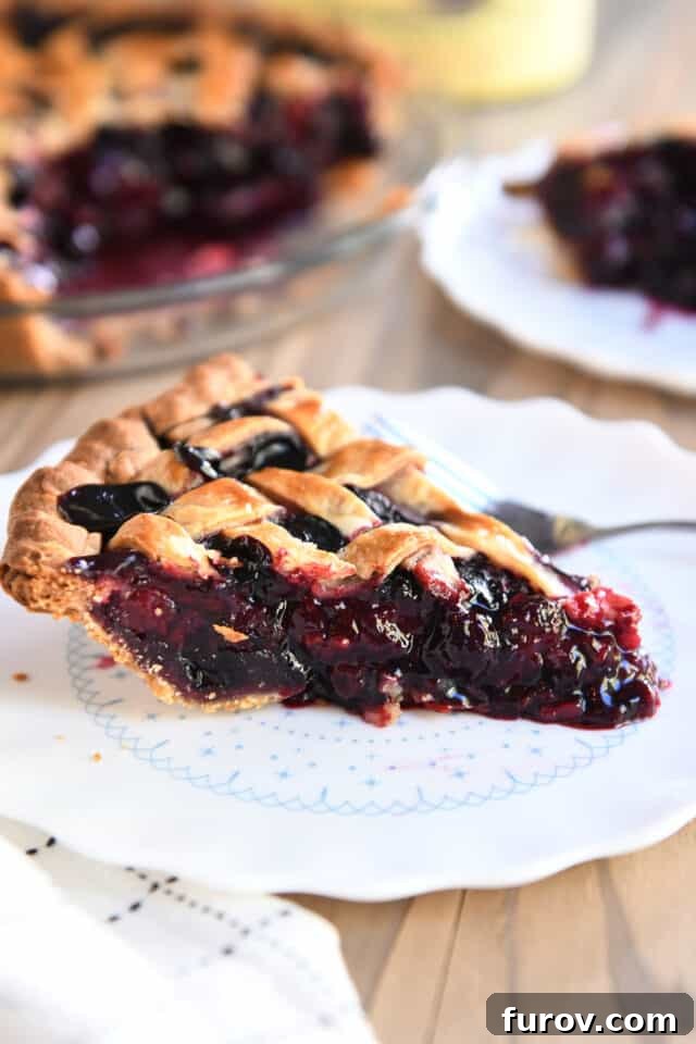 A single, perfectly cut slice of triple berry pie placed on a white scalloped plate, accompanied by a silver fork, highlighting the vibrant filling.