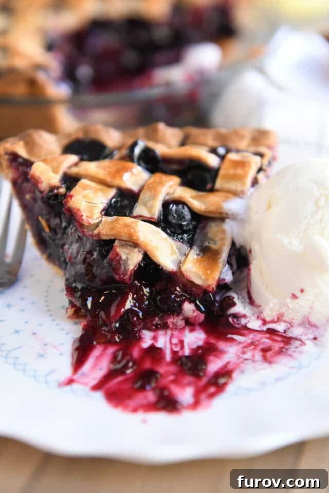 A slice of triple berry pie with a bite removed, served on a white plate with a scoop of creamy vanilla ice cream melting alongside.