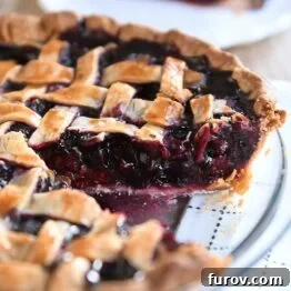 Triple berry pie in glass pie dish with one piece removed.
