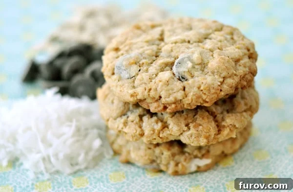 A stack of chocolate chip cookies next to piles of coconut and chocolate chips, showcasing the key ingredients.