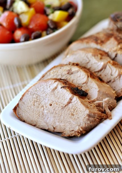 A white rectangular platter with perfectly sliced grilled pork tenderloin, garnished with fresh herbs, positioned next to a vibrant bowl of chopped vegetables and black beans, creating a complete and inviting meal.