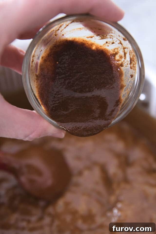 A vanilla and spice paste being poured into hot, cooked caramel, ensuring even distribution of flavor.