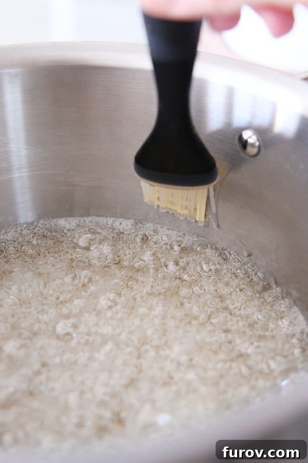 A pastry brush being used to wipe down the inside edges of a saucepan, preventing sugar crystallization during caramel making.