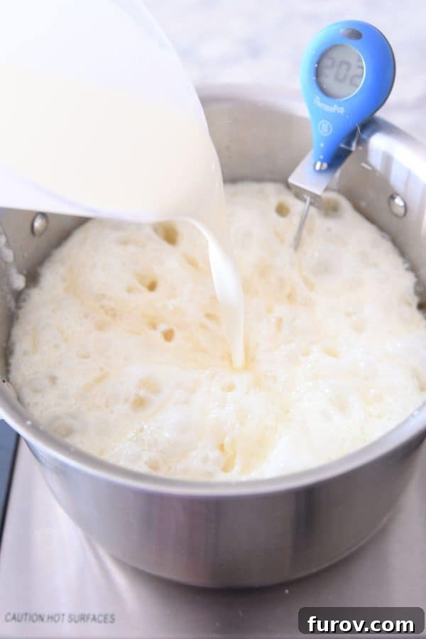 Warm cream, butter, and salt being added to the hot amber sugar mixture in a saucepan, causing it to bubble and steam.