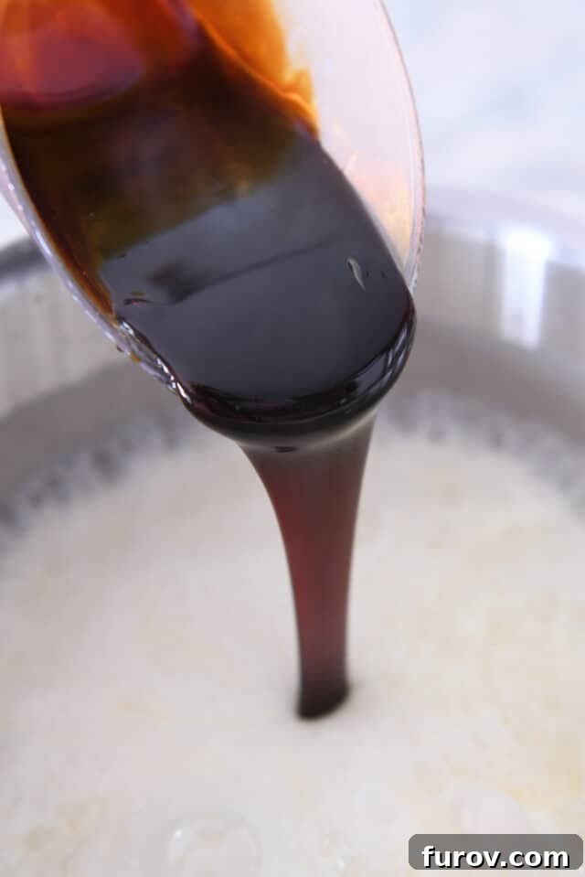 Molasses being poured into the bubbling sugar mixture in a pan, adding depth of color and flavor.