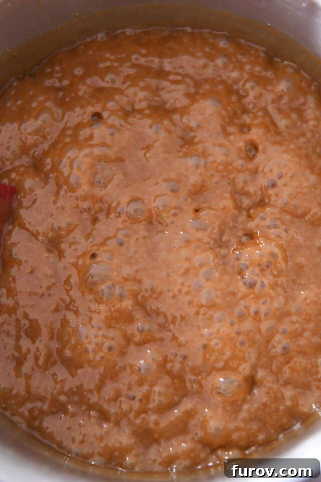 A pot filled with amber-colored hot caramel, the bubbles have grown larger and the mixture has thickened slightly.