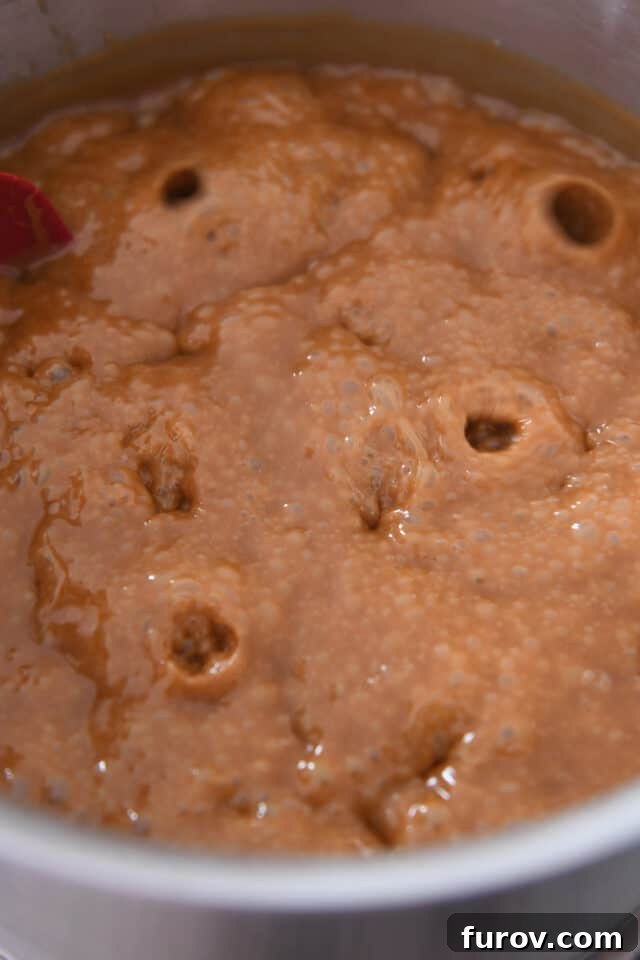 A bubbling pan of hot caramel, now very thick and forming large, slow-moving bubbles on the surface.