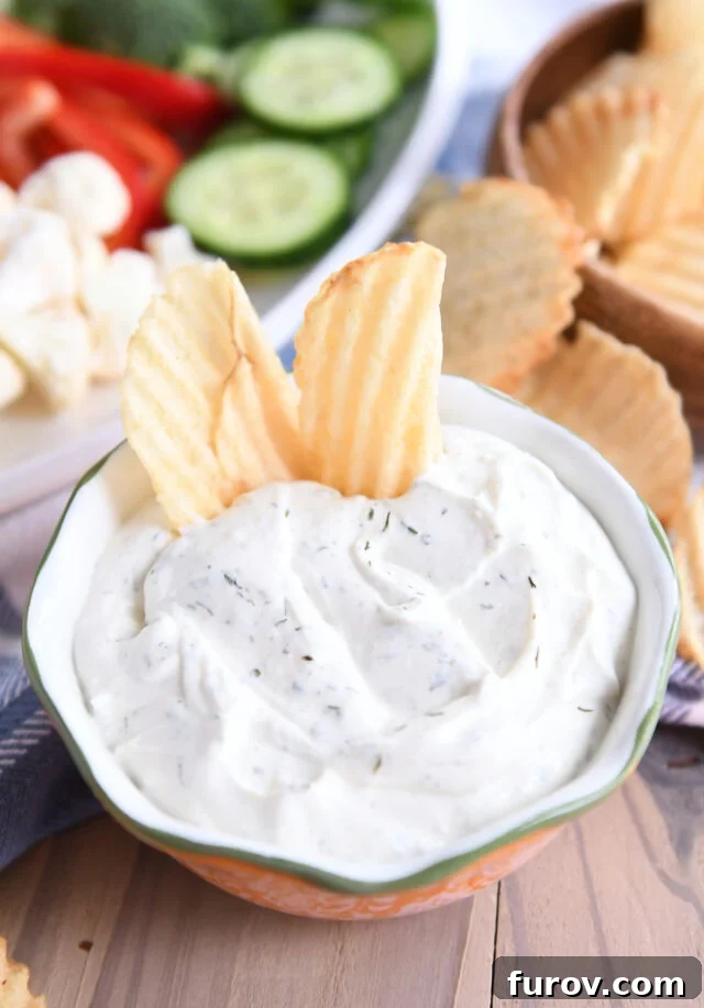 Two golden, wavy potato chips artfully positioned within a generous serving of the creamy veggie dip, showcasing its perfect dipping consistency.