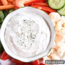 A small glass bowl brimming with creamy veggie dip, elegantly presented on a white tray and surrounded by an assortment of colorful, fresh vegetables.