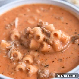 Spoon scooping up bite of soup with tomatoes, noodles, and ground beef.