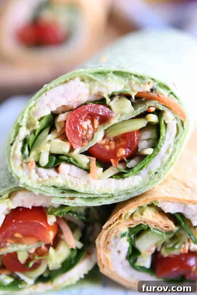 Half of a turkey avocado veggie wrap stacked on two other wraps, showcasing fresh ingredients.