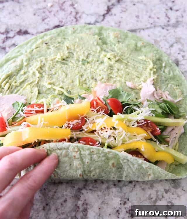 Rolling up a turkey avocado veggie wrap, showing the technique for a tight seal.