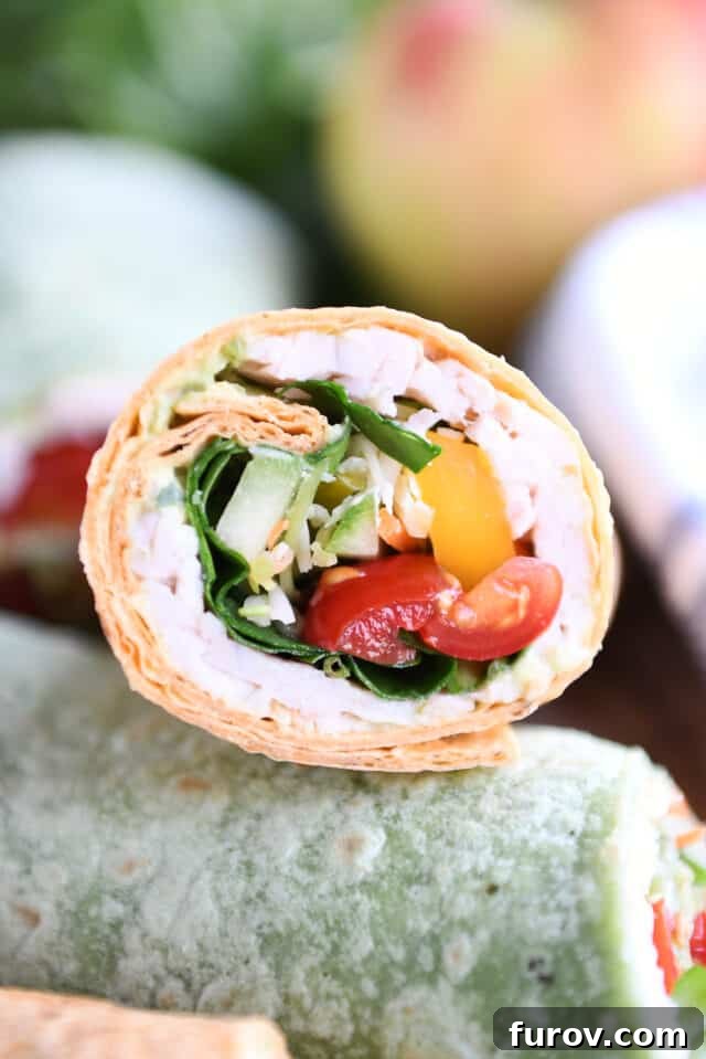 Half of a turkey wrap stuffed with colorful tomatoes, cucumbers, bell peppers, and spinach, showcasing the fresh filling.