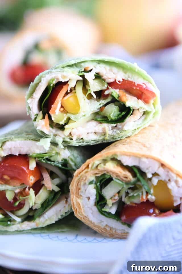 Three perfectly rolled turkey avocado veggie wraps on a white plate, ready to serve.