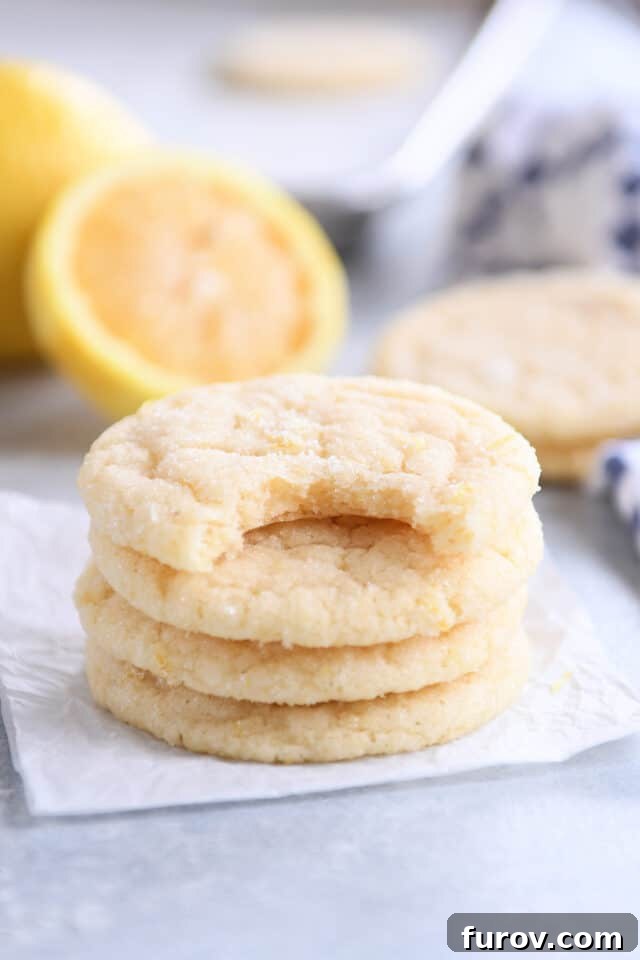 Soft & Chewy Lemon Drop Cookies: So Easy! 2 Three stacked lemon sugar cookies with one on top with bite taken out, showcasing their soft texture and vibrant color.