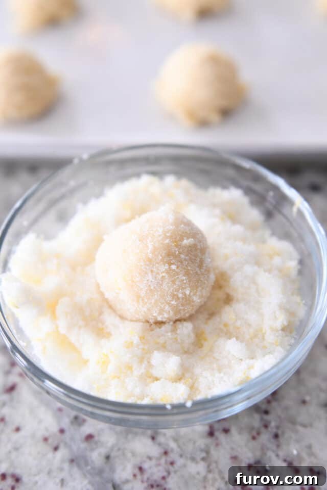 Soft & Chewy Lemon Drop Cookies: So Easy! 5 Hands rolling a ball of sugar cookie dough in lemon sugar, creating a beautiful coating.