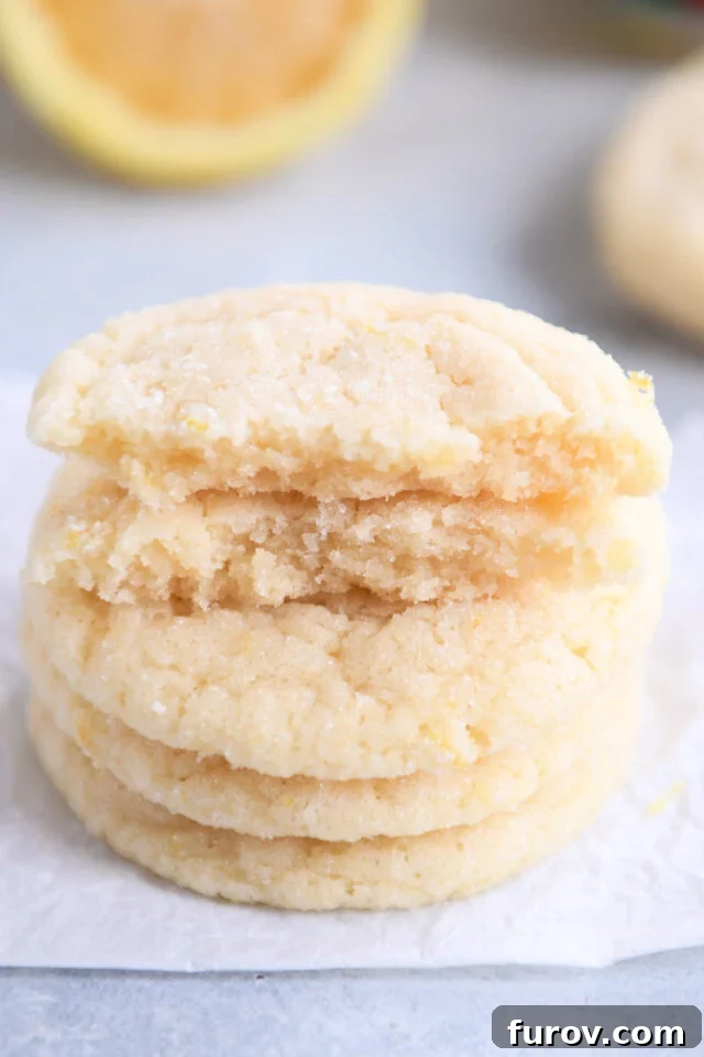 Soft & Chewy Lemon Drop Cookies: So Easy! 7 Close up of two broken cookie halves on top of a stack of golden lemon sugar cookies, highlighting their soft, chewy interior.