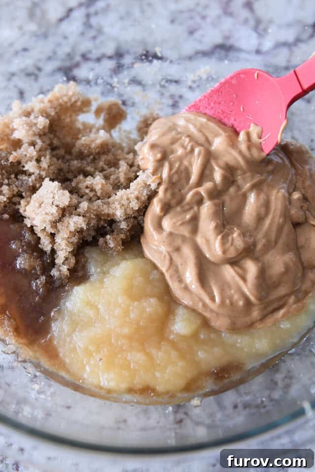 A glass bowl filled with the wet ingredients for the cookie dough, including brown sugar, applesauce, oil, and creamy peanut butter, waiting to be combined.